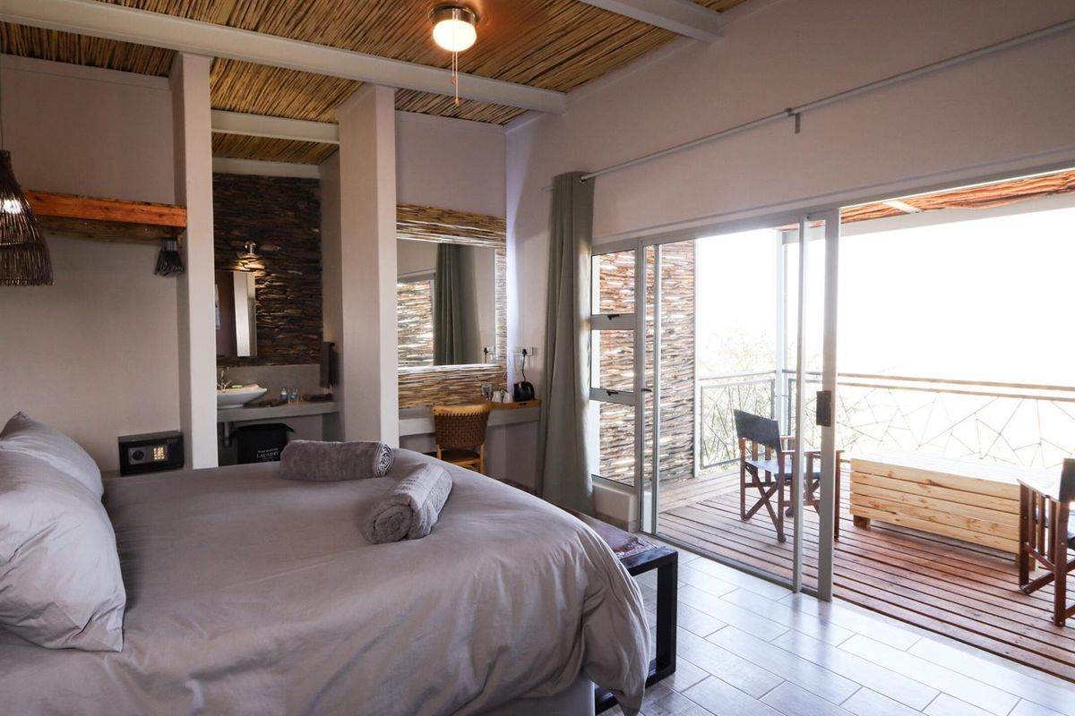 Spacious bedroom featuring a thatched ceiling, en-suite vanity area, and sliding glass doors opening onto a private wooden deck with scenic views.