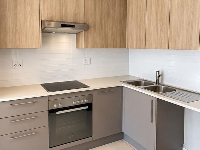 Modern kitchen featuring light wood-tone upper cabinets, grey lower cabinetry, stone countertops, integrated oven, electric hob, and a stainless steel double sink.