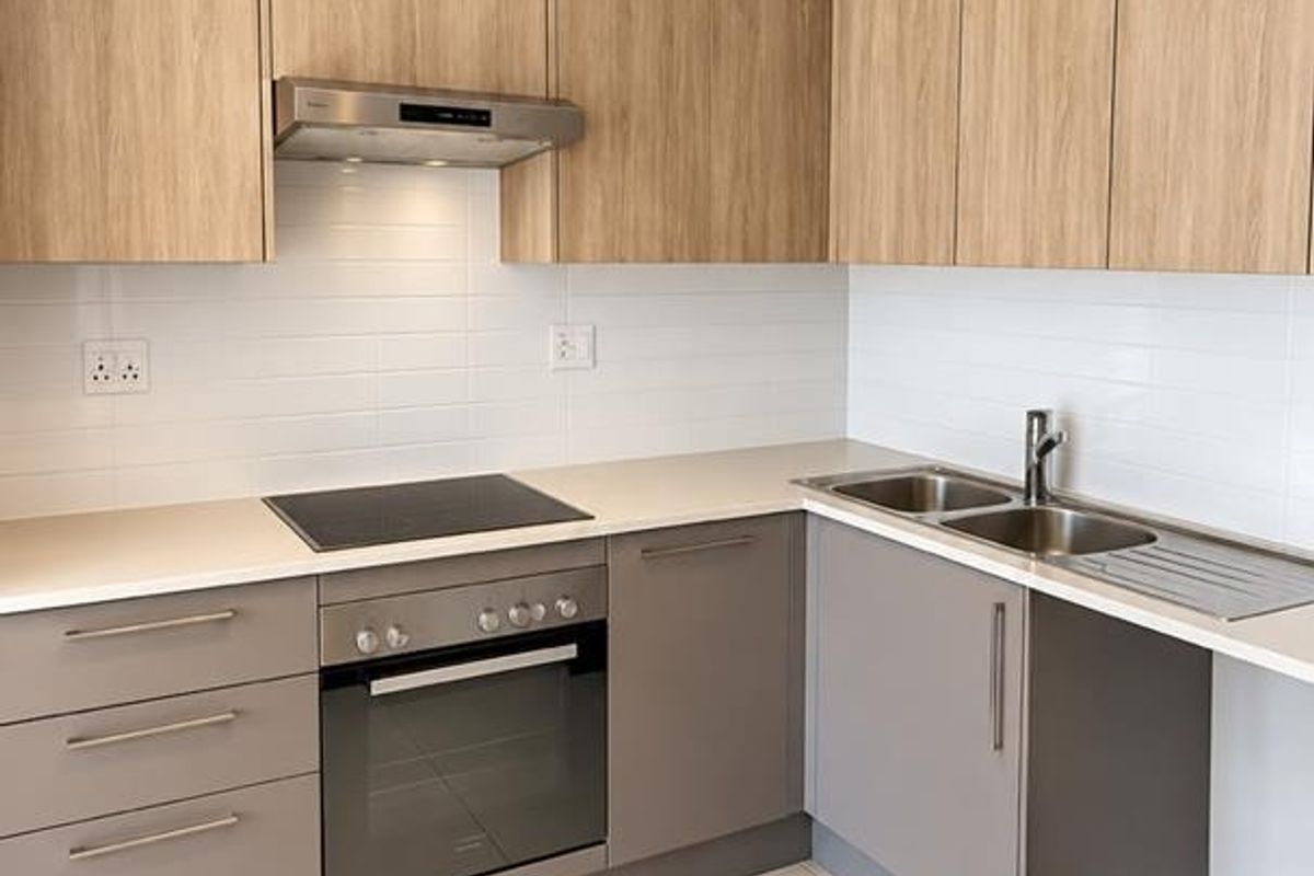 Modern kitchen featuring light wood-tone upper cabinets, grey lower cabinetry, stone countertops, integrated oven, electric hob, and a stainless steel double sink.