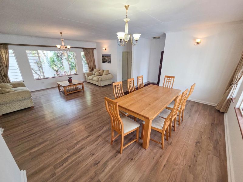 Spacious open-plan living and dining area featuring modern laminate flooring, ample natural light from large windows, and elegant chandelier lighting.