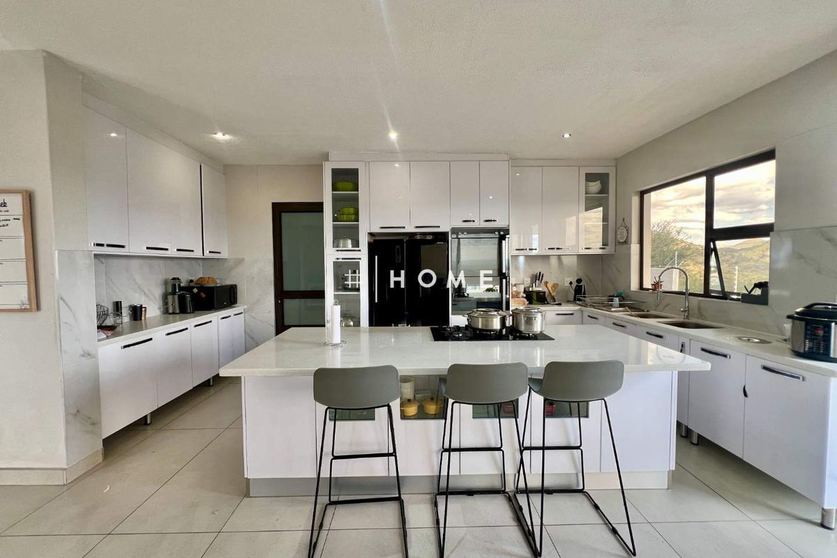 Modern kitchen featuring white cabinetry, a central island with a built-in cooktop, stone countertops, and large windows providing natural light.