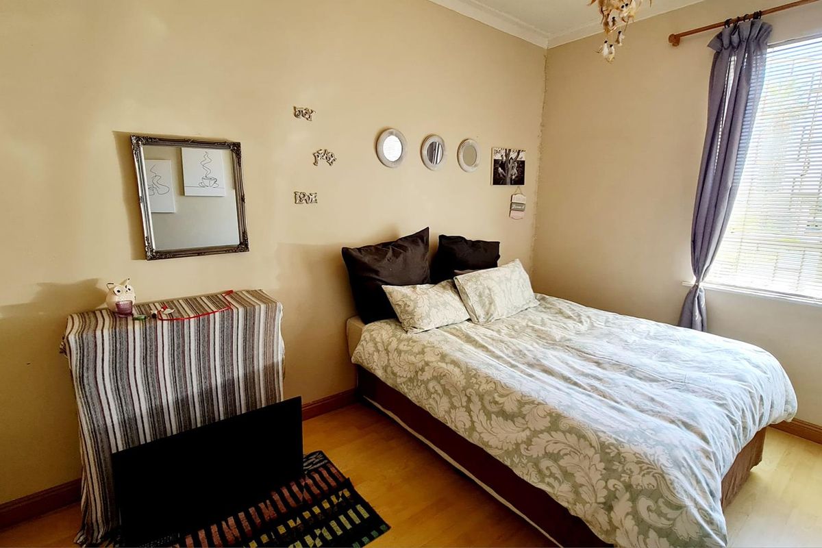 A bedroom featuring laminate flooring, a window with fitted blinds, and neutral wall finishes.