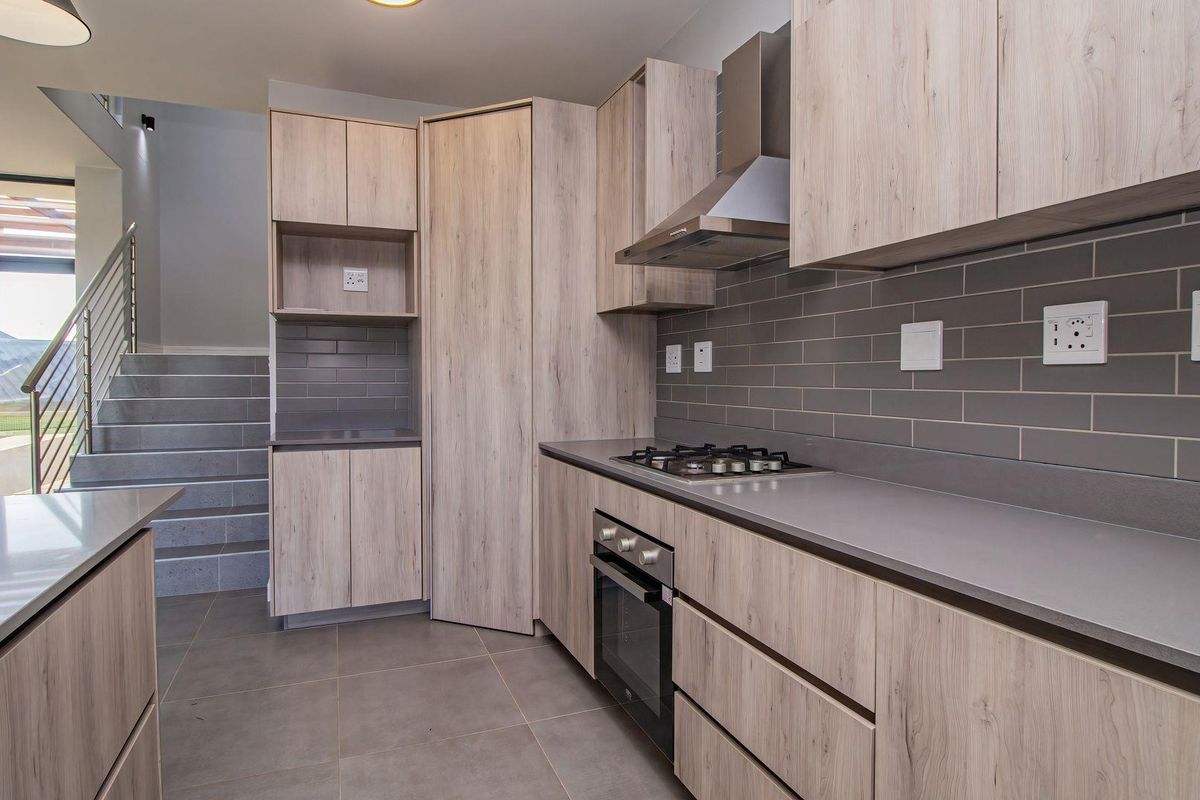 Modern kitchen featuring light wood-grain cabinetry, stone countertops, subway tile backsplash, built-in oven, gas hob, and stainless steel extractor fan.
