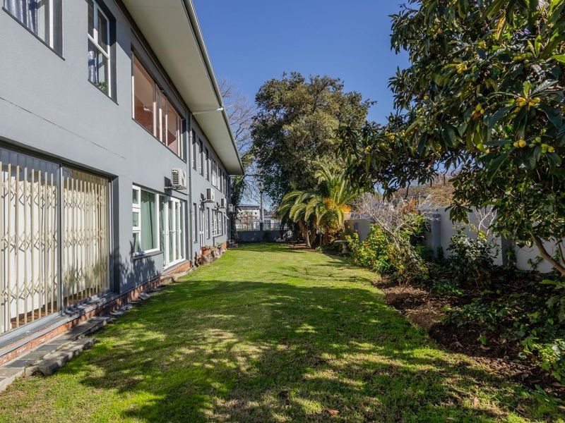 A well-maintained rear garden area featuring a lawn, mature trees, and direct access to the apartment via sliding glass doors with security gates.