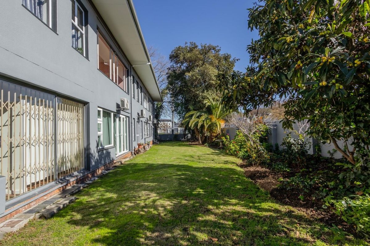 A well-maintained rear garden area featuring a lawn, mature trees, and direct access to the apartment via sliding glass doors with security gates.