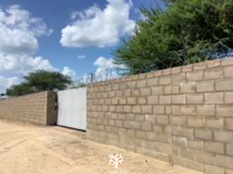 A view of the commercial property boundary featuring a concrete block perimeter wall, a secure sliding gate, and installed razor wire security.