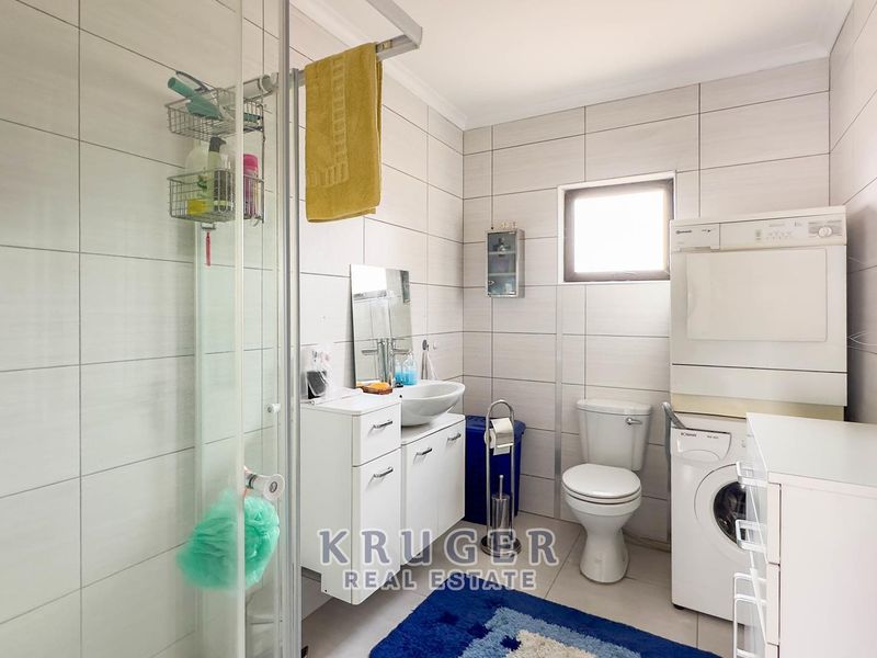 A functional bathroom featuring a glass shower enclosure, vessel sink with vanity, toilet, and integrated laundry facilities with tiled finishes throughout.