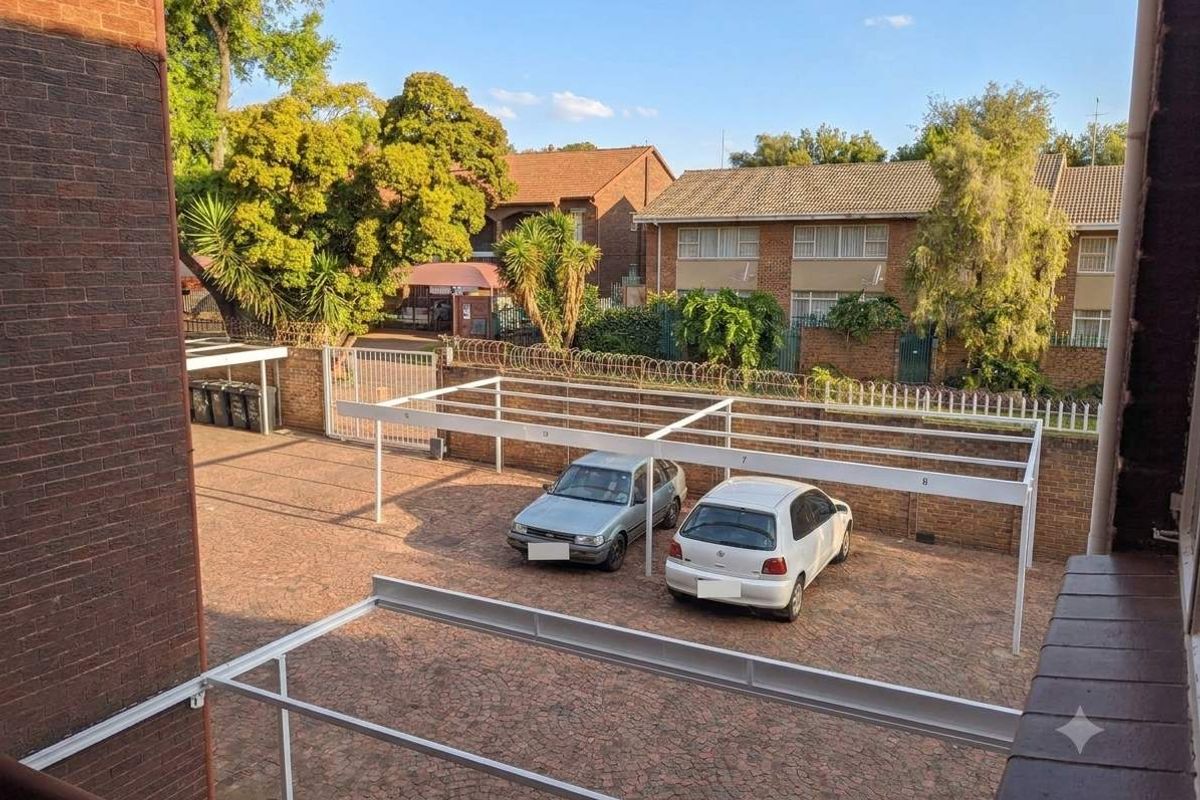 An elevated view of the apartment complex rear parking area featuring paved surfaces and covered carport structures.
