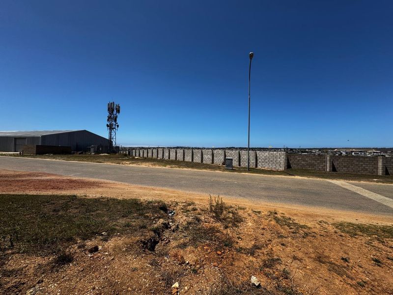 Street view of the industrial property featuring a concrete block boundary wall, telecommunications tower, and asphalt road access.