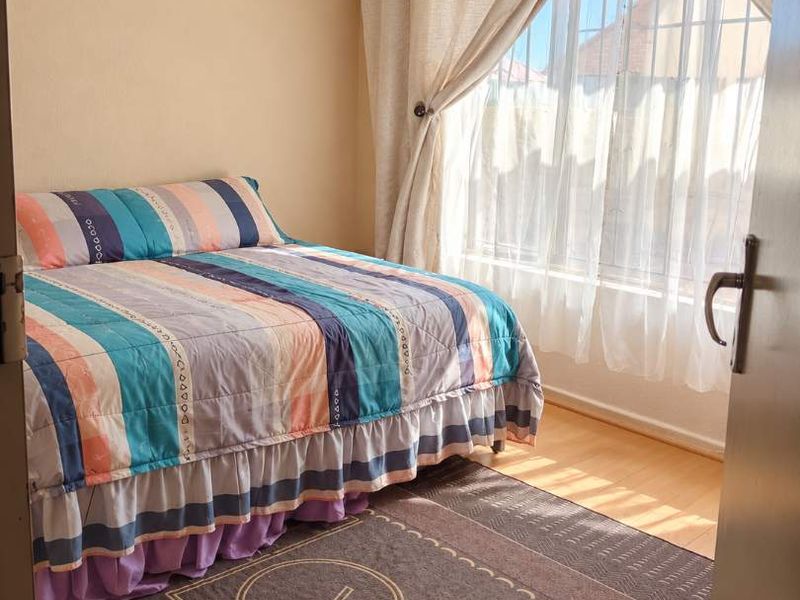 A functional bedroom featuring laminate flooring and a window fitted with security bars, allowing for natural light.