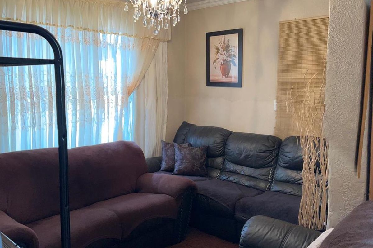A cozy living room featuring a decorative crystal chandelier, textured wall finishes, and large windows with layered curtains.