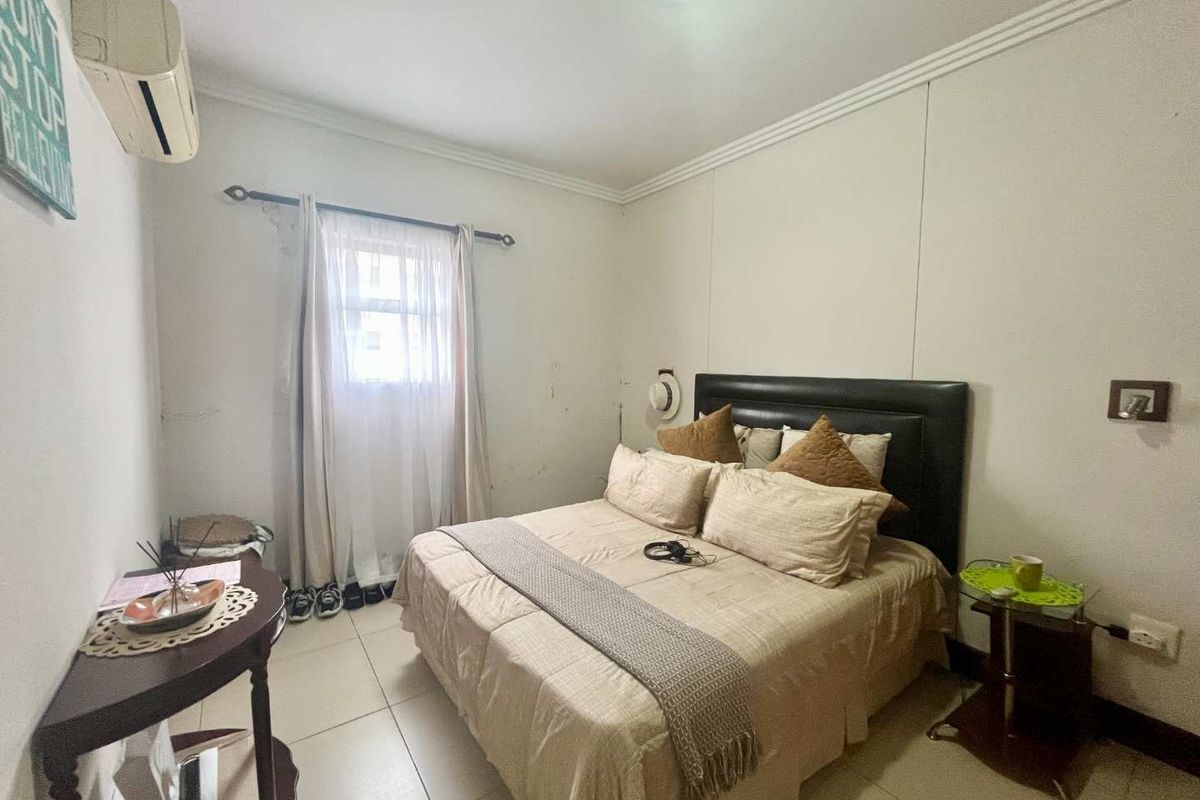A functional bedroom featuring tiled flooring, a wall-mounted air conditioning unit, and a window with curtain rod.