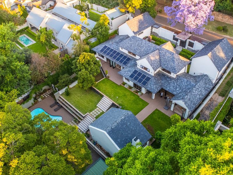 Aerial view of a well-maintained residential property featuring a slate roof, solar panels, landscaped gardens, a swimming pool, and multi-level paved patio areas.