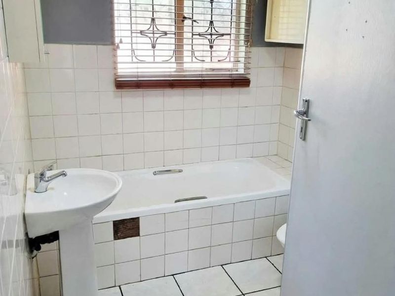 A compact bathroom featuring a pedestal basin, a built-in bathtub with tiled surround, and tiled flooring, requiring minor maintenance and cosmetic updates.