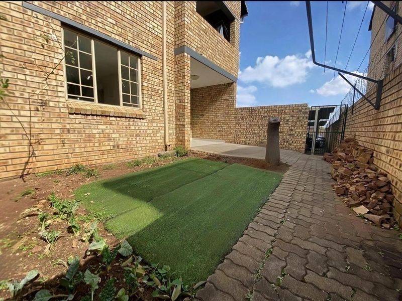 Rear exterior view of the apartment building featuring a face brick facade, paved walkway, and a small garden area with artificial grass.