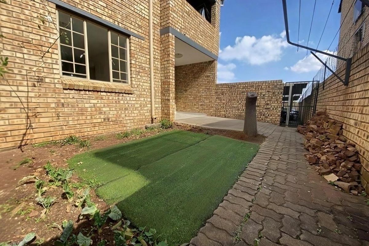 Rear exterior view of the apartment building featuring a face brick facade, paved walkway, and a small garden area with artificial grass.