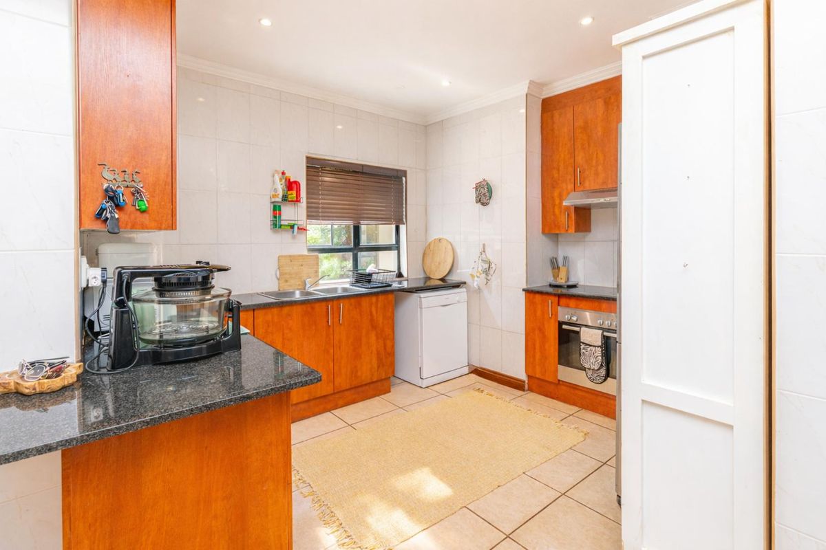 A functional kitchen featuring wood-finish cabinetry, granite countertops, a built-in oven with extractor fan, and tiled flooring throughout.