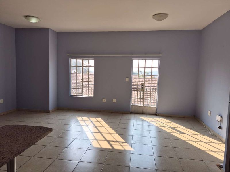 A spacious, empty living area featuring tiled floors, natural light through grid-pattern windows, and a breakfast bar, ready for personalization.