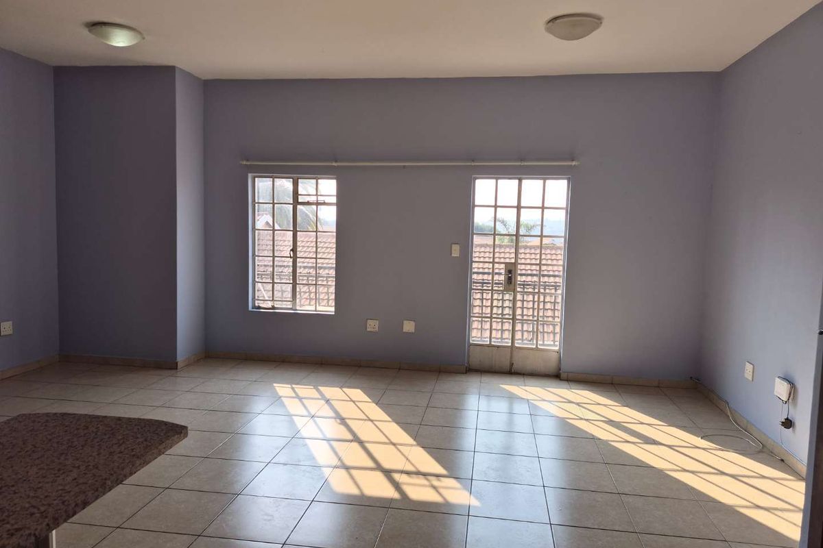A spacious, empty living area featuring tiled floors, natural light through grid-pattern windows, and a breakfast bar, ready for personalization.