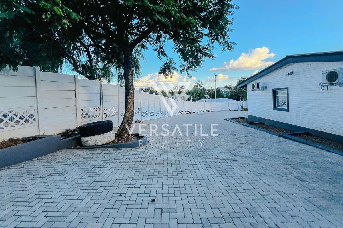 Exterior view of the property featuring paved driveway, perimeter walling, and exterior air conditioning units.