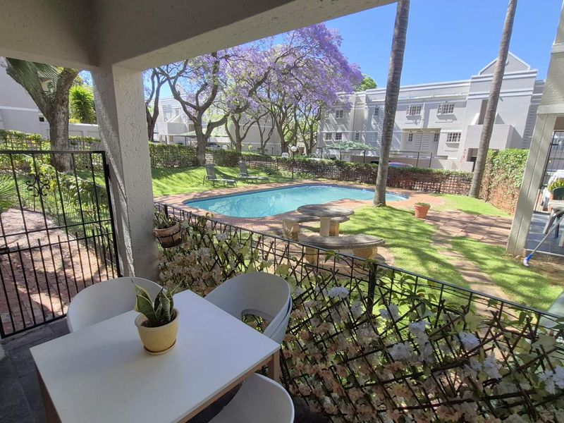 A covered patio overlooking a communal swimming pool and landscaped garden area within the apartment complex.