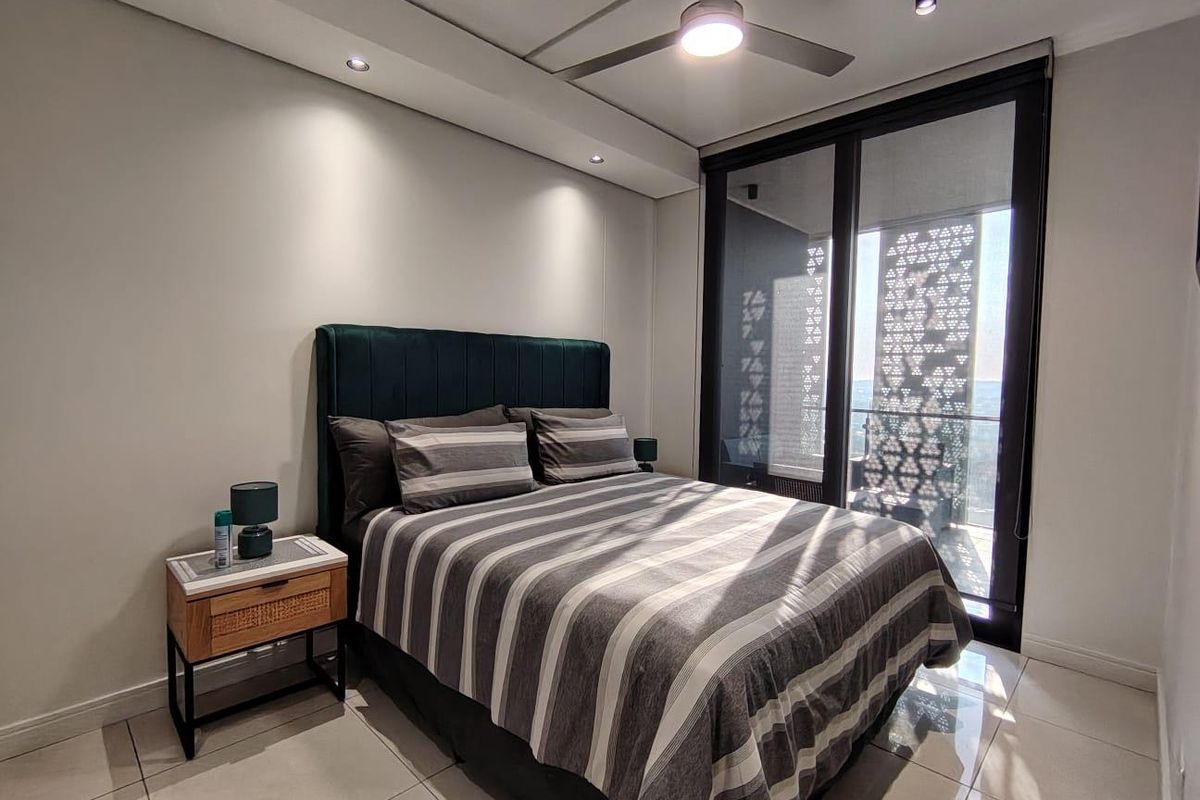 Modern bedroom featuring tiled flooring, recessed lighting, a ceiling fan, and large sliding glass doors providing access to a private balcony with decorative screening.