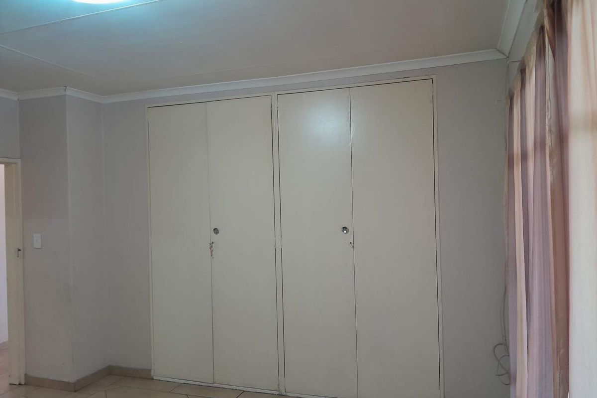 A bedroom featuring built-in cupboards and tiled flooring, offering a neutral space ready for personalization.
