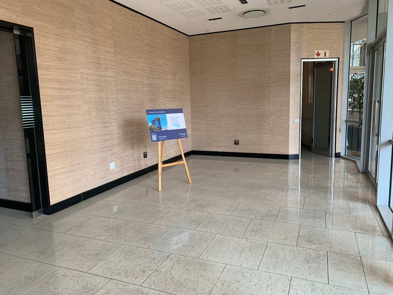 A bright, modern office space featuring polished tile flooring, wood-look wall paneling, and large glass windows providing ample natural light.
