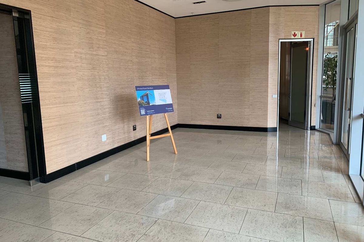 A bright, modern office space featuring polished tile flooring, wood-look wall paneling, and large glass windows providing ample natural light.