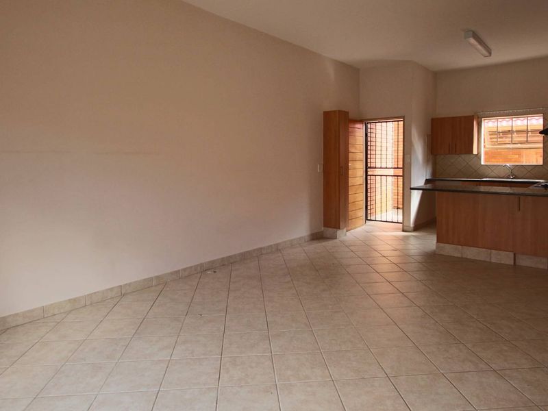 Open plan living area featuring tiled floors and a functional kitchen with built-in cabinetry, hob, and oven, leading to an exterior security gate.
