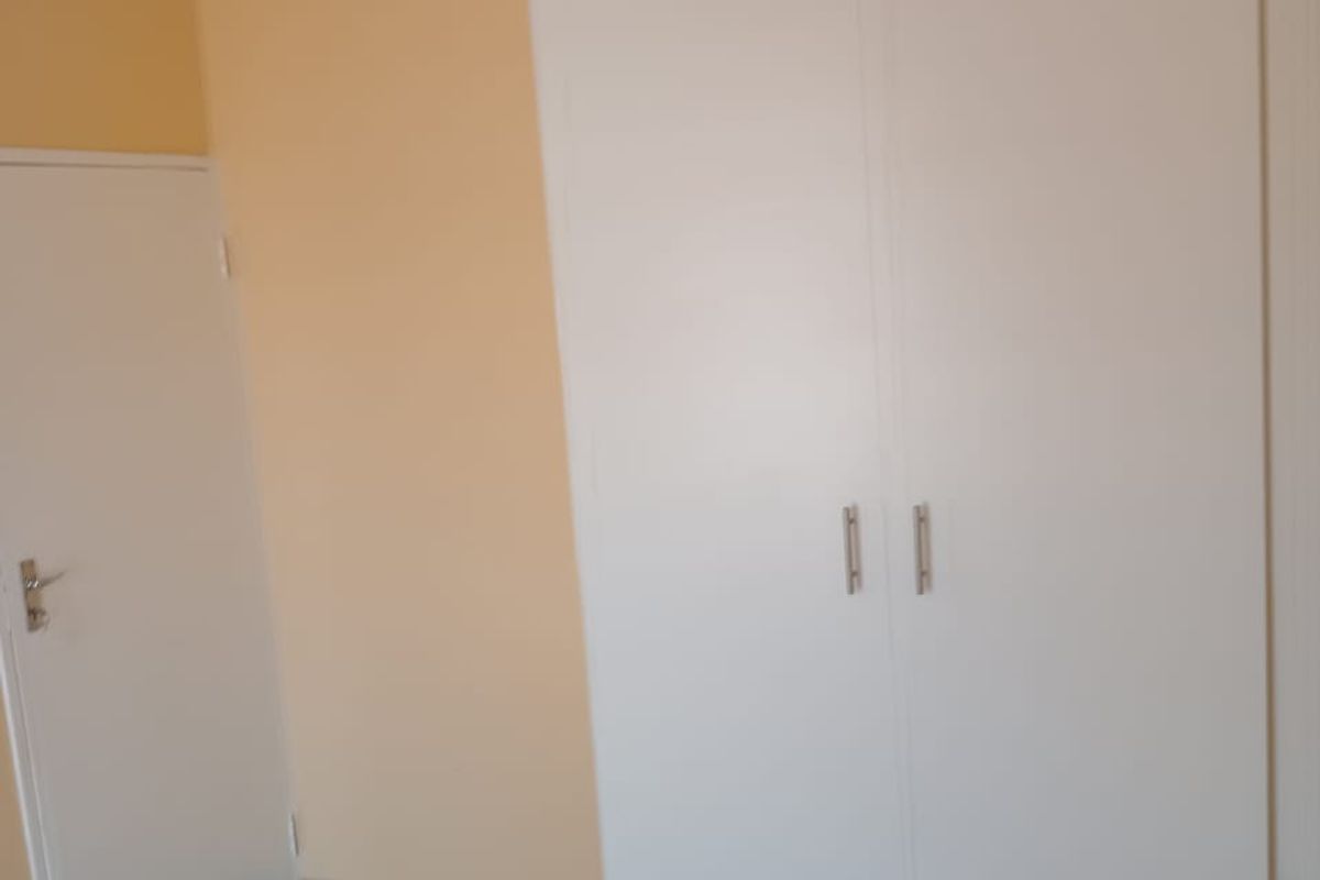 A clean bedroom featuring neutral walls, tiled flooring, and a white built-in wardrobe.