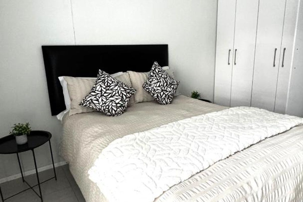 A bright bedroom featuring neutral tiled flooring and built-in floor-to-ceiling white cabinetry for ample storage.