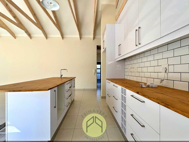 Modern kitchen featuring white cabinetry, wooden countertops, subway tile backsplash, and striking exposed timber ceiling beams in an open-plan layout.