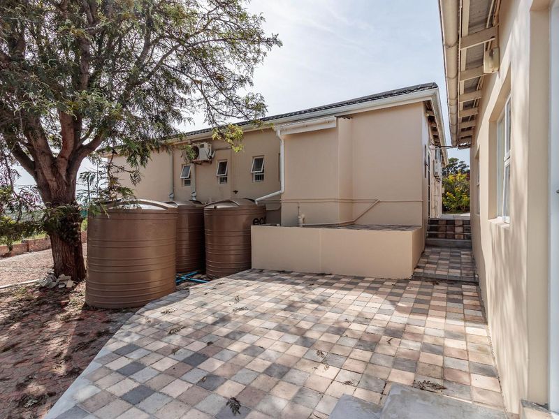 Rear exterior view featuring a paved patio area, multiple water storage tanks, and external building infrastructure including guttering and air conditioning units.
