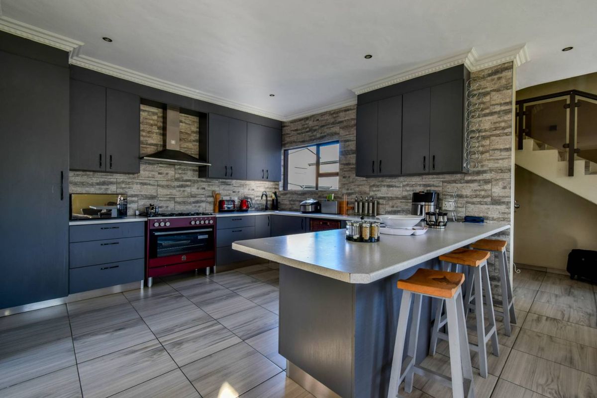 Modern kitchen featuring dark cabinetry, a central island, stone-look wall tiles, and integrated lighting, providing a functional and stylish culinary space.