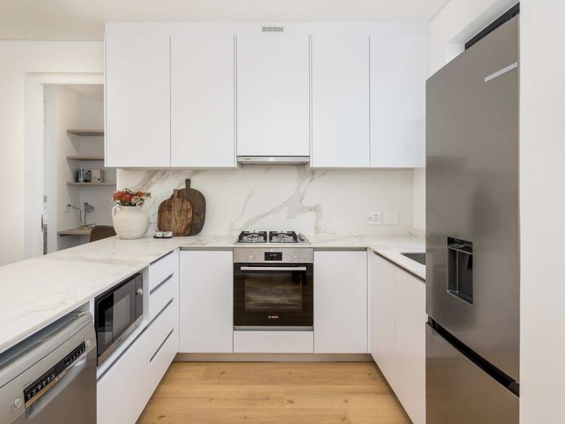 Modern kitchen featuring white cabinetry, marble-look stone countertops and backsplash, built-in oven, gas hob, and integrated appliances.