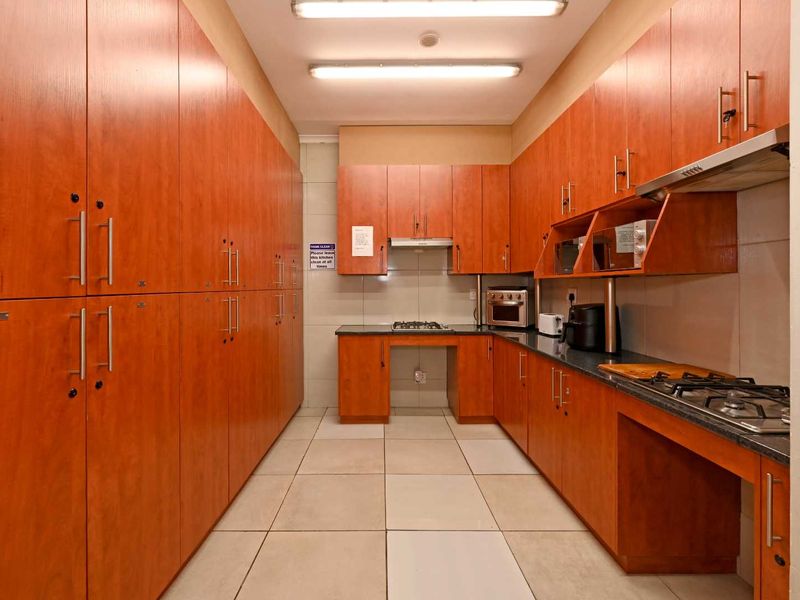 A functional galley-style kitchen featuring extensive wood-finish cabinetry, granite countertops, and integrated gas hobs with overhead extractor fans.