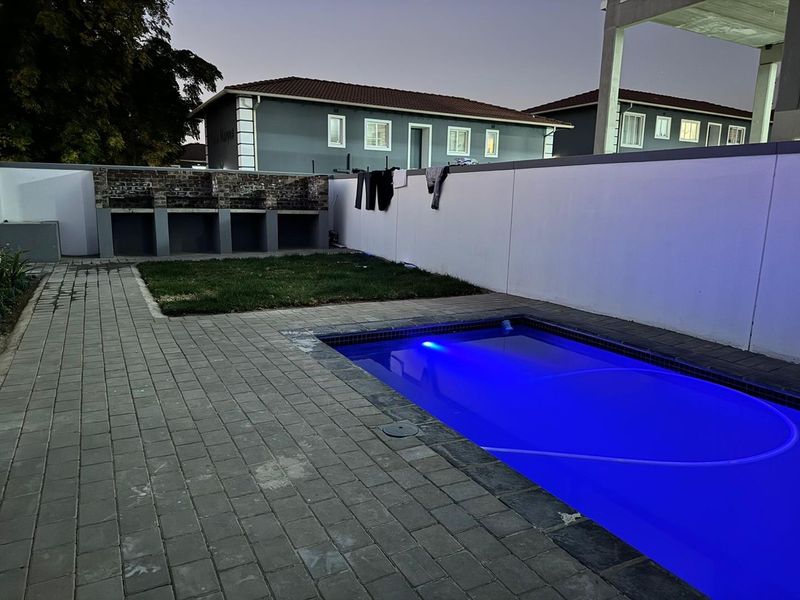 Outdoor pool area featuring a swimming pool, paved surround, and a built-in brick braai facility against the boundary wall.