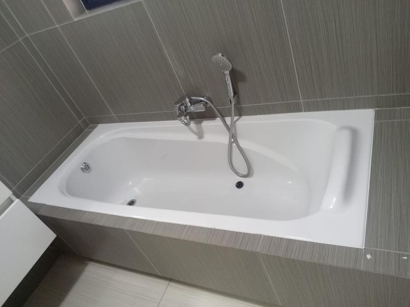 A clean, modern bathroom featuring a built-in bathtub with chrome fixtures and neutral grey wall tiling.