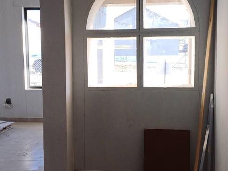An unfinished interior space featuring tiled flooring, an arched window, and recessed lighting, currently in a state of renovation.