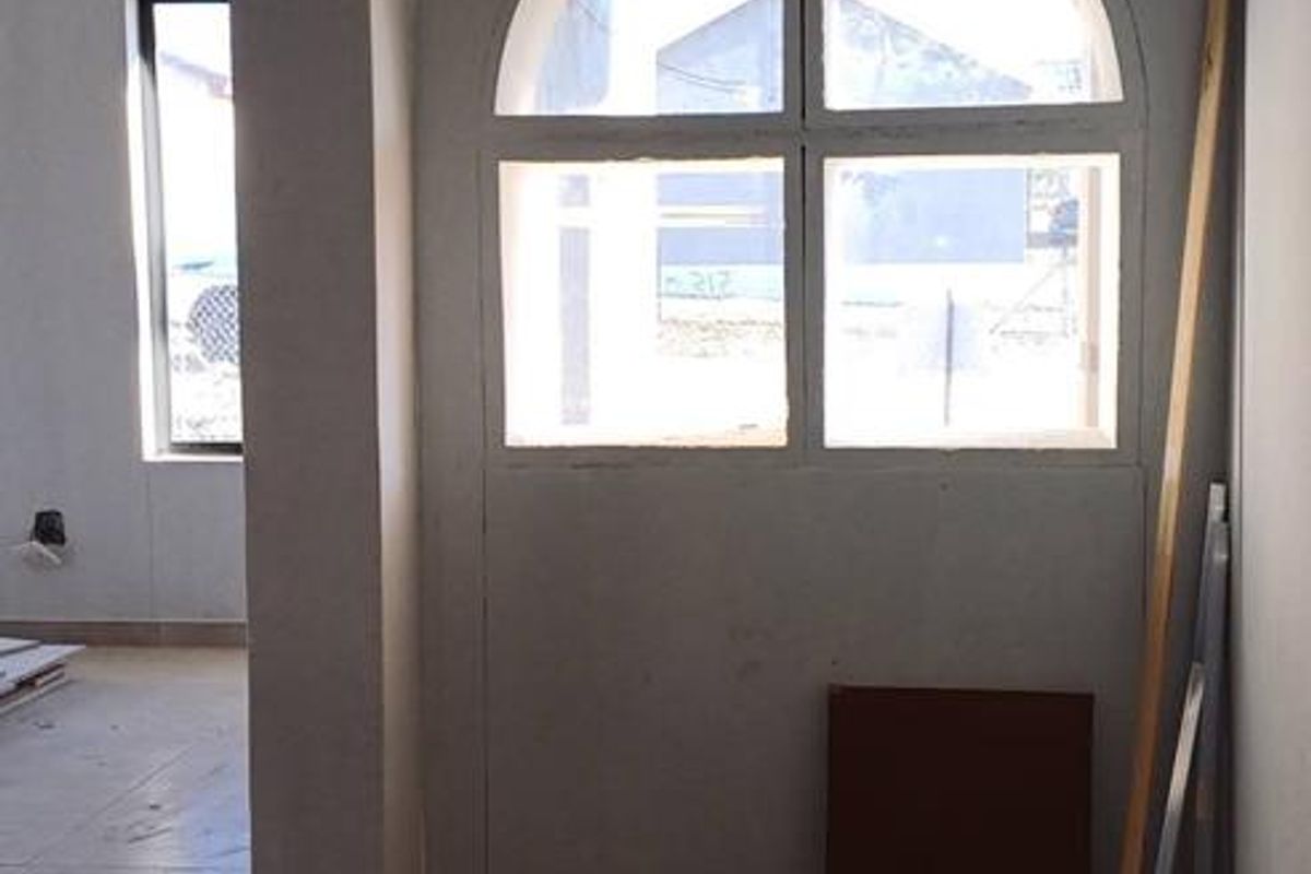 An unfinished interior space featuring tiled flooring, an arched window, and recessed lighting, currently in a state of renovation.