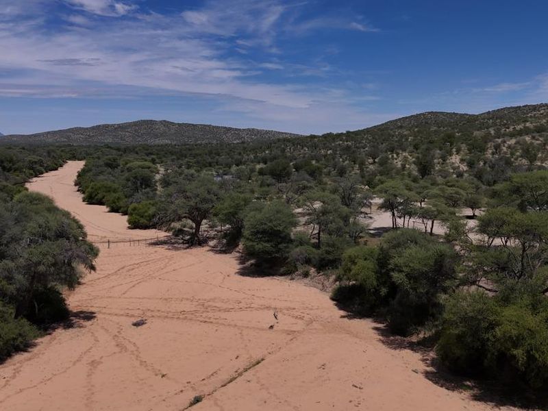 An aerial view of the farm property featuring a dry riverbed, natural landscape, and established indigenous trees under a clear blue sky.