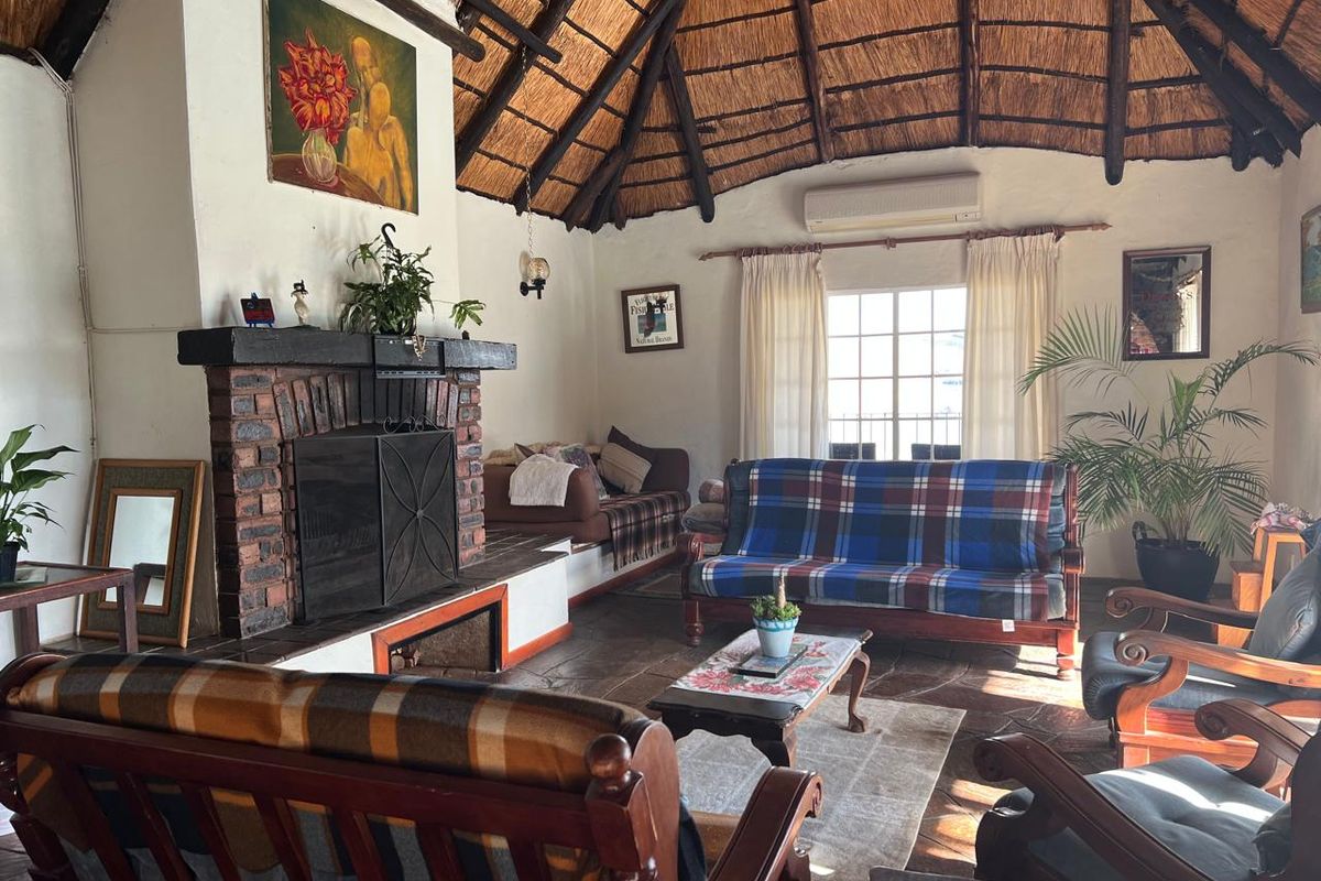 Spacious living room featuring a traditional thatched roof, exposed brick fireplace, and stone flooring, creating a rustic and cozy atmosphere.