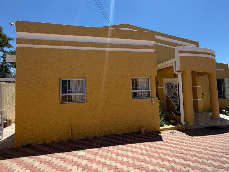 Front elevation of a house featuring a textured yellow facade, paved driveway, and a covered entrance porch with security gate.