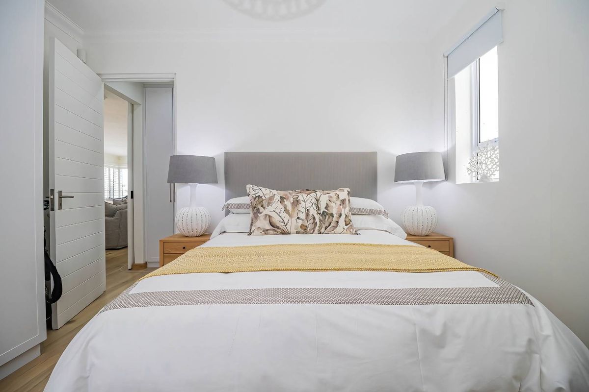 A well-maintained bedroom featuring light laminate flooring, a built-in wardrobe, and a window with a roller blind, offering a clean and neutral living space.