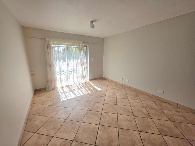 A bright, empty living room featuring neutral tiled flooring and a sliding glass door providing natural light and access to the exterior.