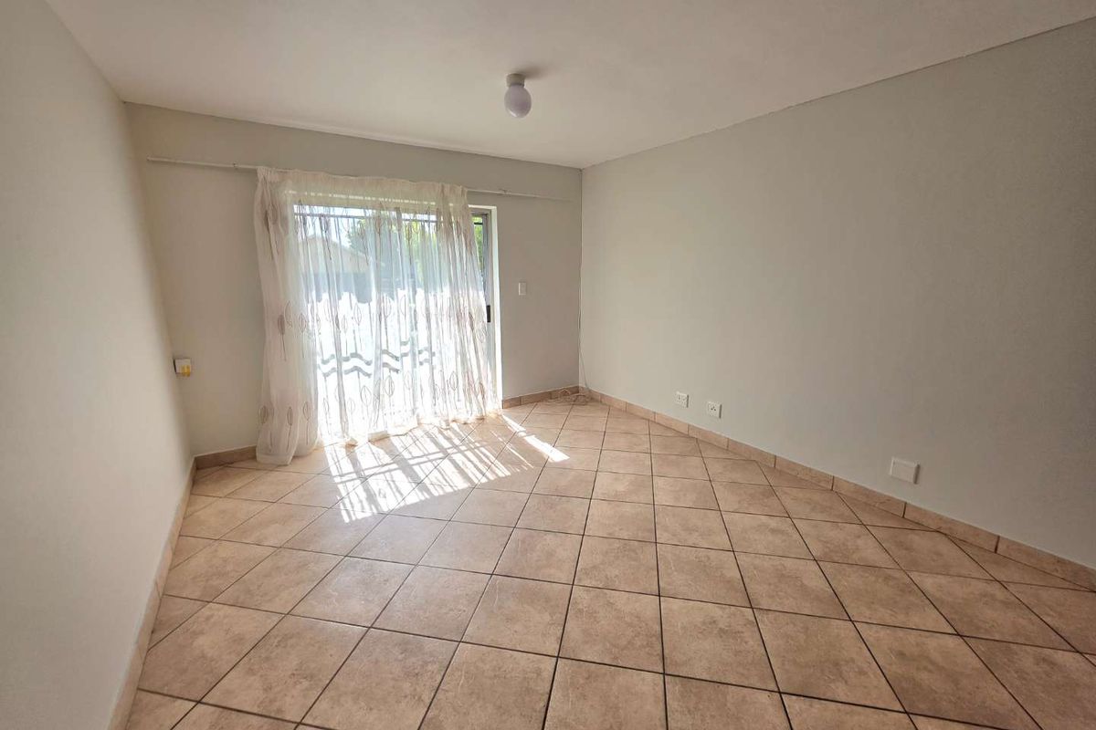 A bright, empty living room featuring neutral tiled flooring and a sliding glass door providing natural light and access to the exterior.