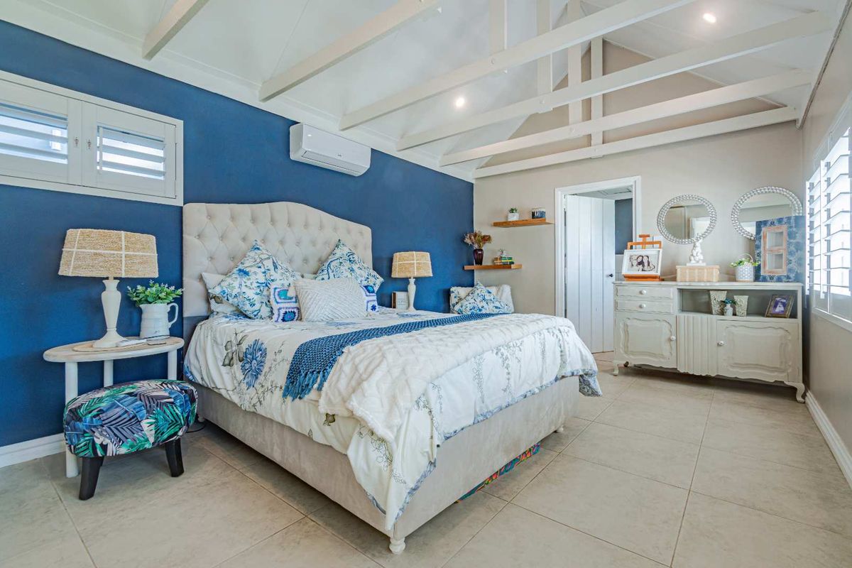 Spacious bedroom featuring vaulted ceilings with exposed beams, tiled flooring, plantation shutters, and a split-system air conditioning unit.