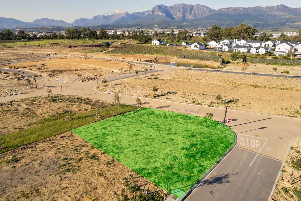 Aerial view of a vacant residential plot in a developing estate, featuring road access and scenic mountain views in the background.