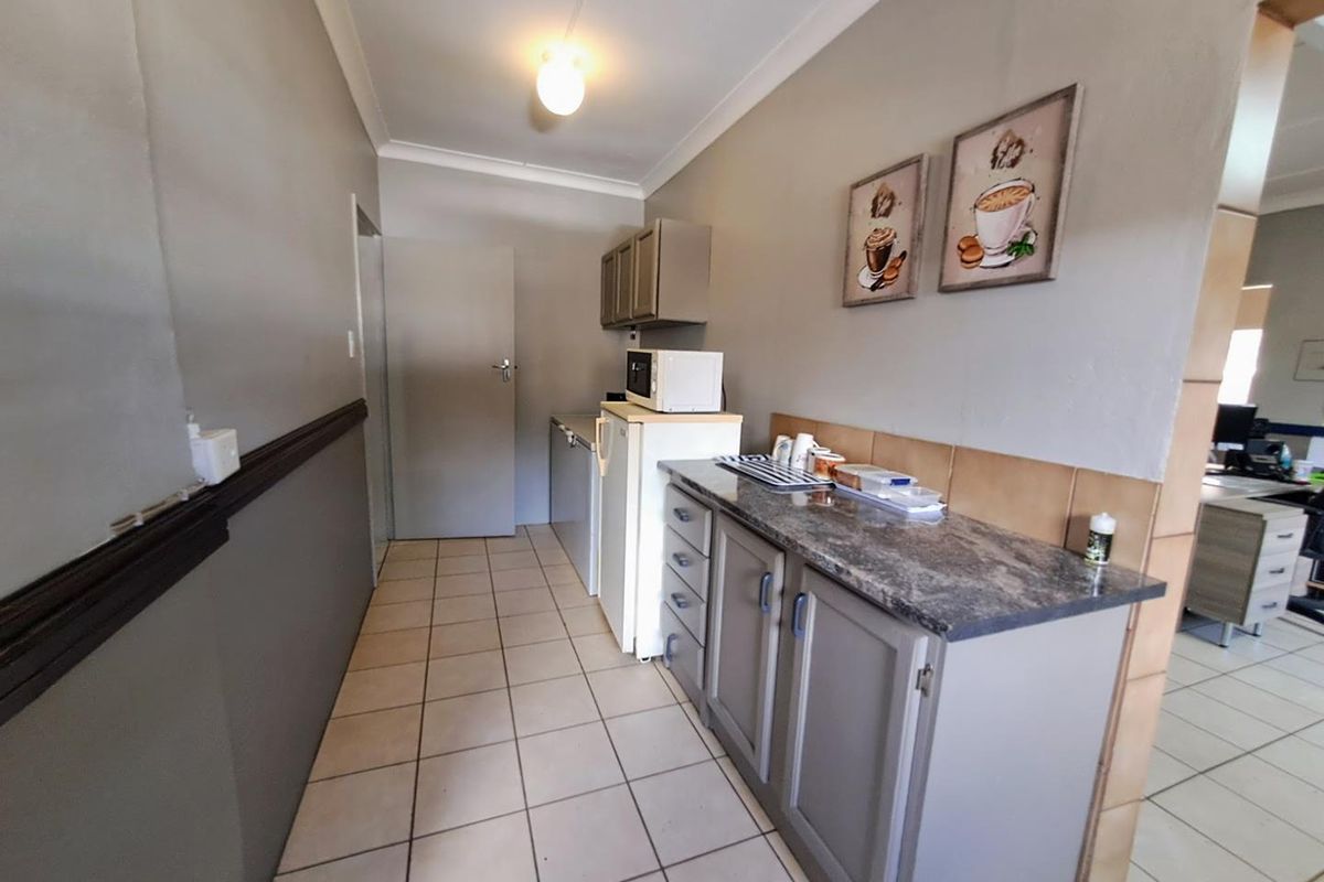 A functional office kitchenette area featuring built-in cabinetry, stone-look countertops, tiled flooring, and a tiled backsplash.